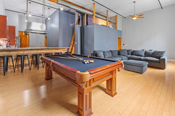 A pool table with a wooden finish, a bar area with stools, and a gray sofa in a modern living space. - Best Location for Conventions, Sports, & Nightlife (Indianapolis)