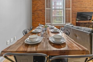 A dining area with a long wooden table set for six, flanked by a sofa and a television. - Best Location for Conventions, Sports, & Nightlife (Indianapolis)