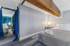 A hotel room with a bed, a nightstand, a lamp, a window with curtains, and a wooden beam above the bed. - Best Location for Conventions, Sports, & Nightlife (Indianapolis)