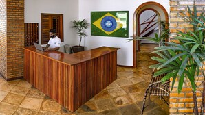 Un mostrador de recepción con detalles de madera, un mural con la bandera de Brasil y una pared de ladrillo.