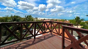 Una terraza de madera con baranda de metal que da a una playa y palmeras.