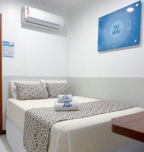 Ein Hotelzimmer mit einem Bett, gestreiften Kissen, einer Wand-Klimaanlage und einem blauen Schild mit der Aufschrift 'EU SOU' an der Wand.