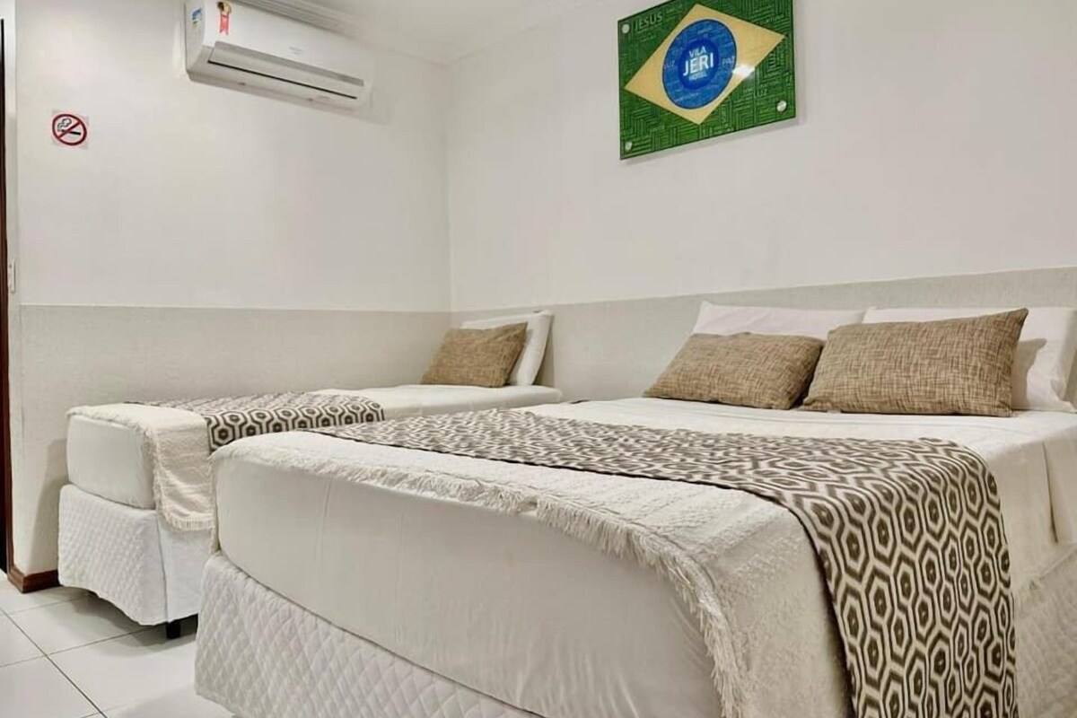 Habitación de hotel con dos camas, aire acondicionado de pared, cartel de no fumar y una bandera brasileña.