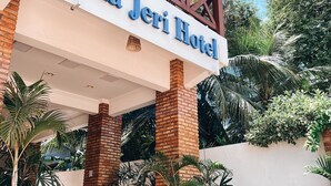 Exterior del Hotel Vila Jeri con un letrero, pilares de ladrillo, plantas en macetas y mesas al aire libre.