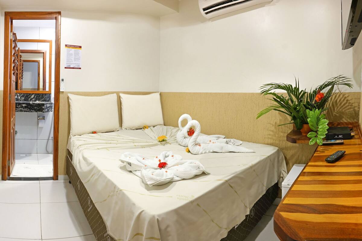 Hotelkamer met een bed, een houten nachtkastje, een potplant en een douchecel.