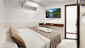 Habitación de hotel con cama, aire acondicionado de pared, un cuadro de paisaje y estante de madera.