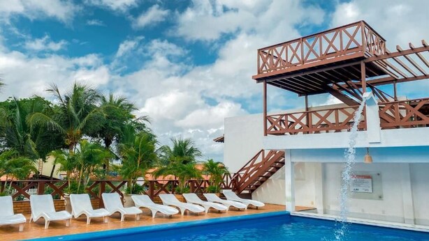 Una piscina con sillas de descanso blancas, una fuente de agua y una estructura de madera para el deck.