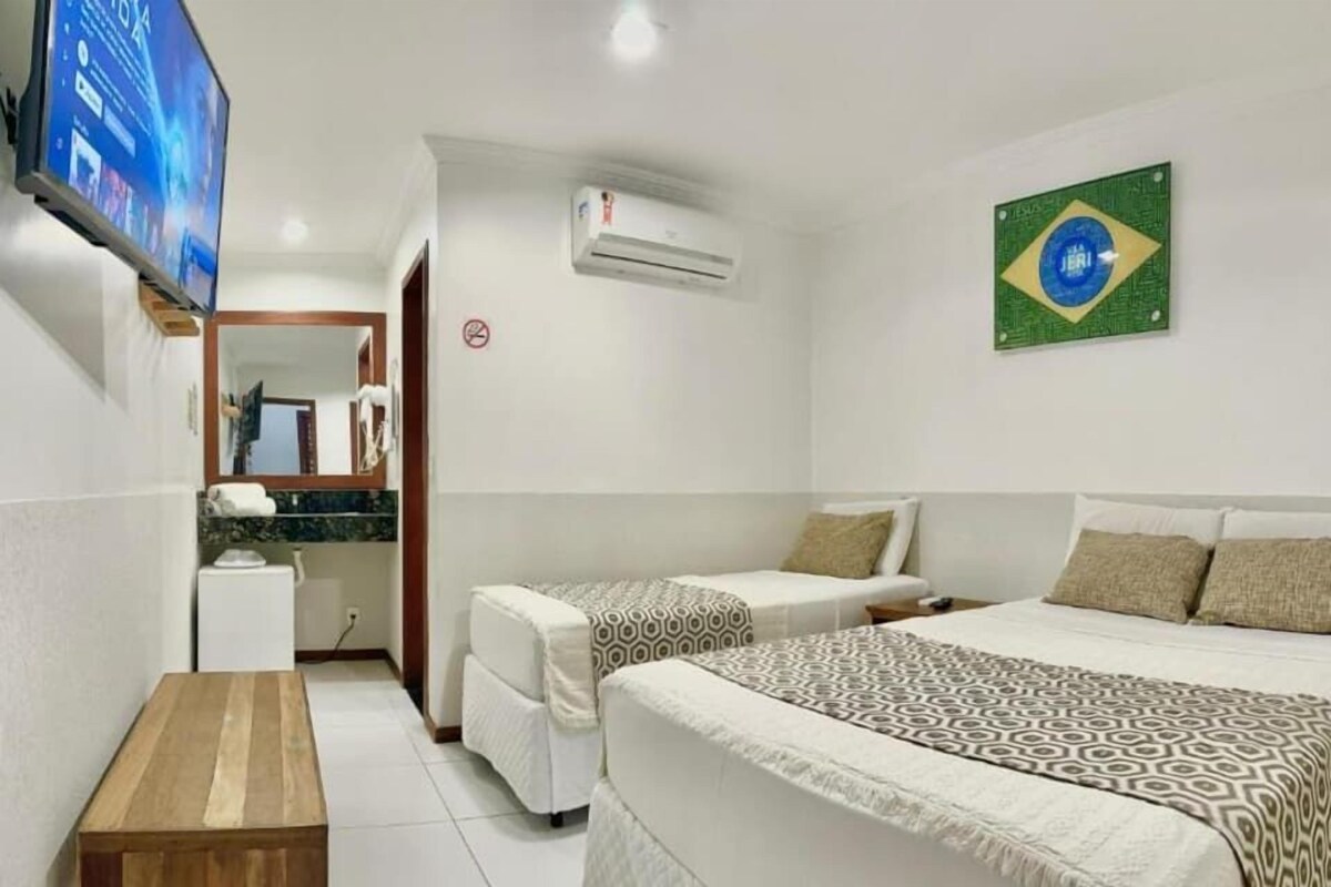 Habitación de hotel con dos camas, un televisor, una mesita pequeña y una decoración con la bandera de Brasil.
