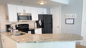 A modern kitchen with white cabinets, a black refrigerator, a stainless steel microwave, a sink, and a countertop. There are two green chairs at the island.