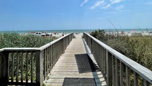 A wooden boardwalk leading to a beach with a clear sky.