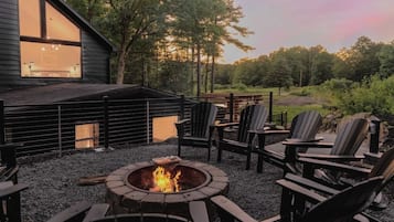 Un espace extérieur accueillant, aménagé avec des fauteuils Adirondack et un foyer, entouré d’une terrasse en bois et d’un sol en gravier.