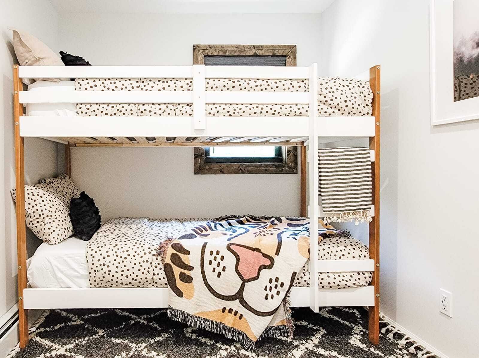 Uma cama beliche com edredom estampado em bolinhas e pelo de leopardo, uma pequena janela e um tapete com padrão preto e branco.