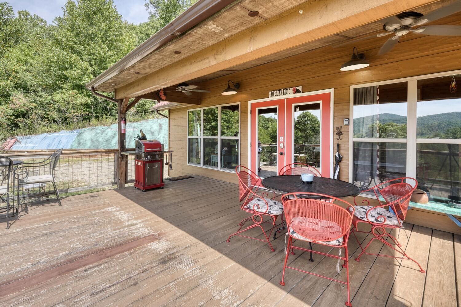 Eine Terrasse im Freien mit Holzdeck, roten Metallstühlen, einem Grill und Blick auf die umliegende Landschaft.