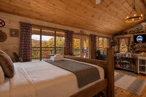 A cozy cabin room with a large bed, wooden walls, and a view of autumn foliage. - Couple's retreat! Studio cabin w/mountain views (Suches)