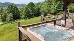 Ein Whirlpool auf einer Holzterrasse mit Blick auf eine grüne Landschaft und Berge.