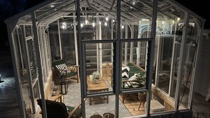 A greenhouse with a glass roof, wooden flooring, and a dining area with chairs and a table.