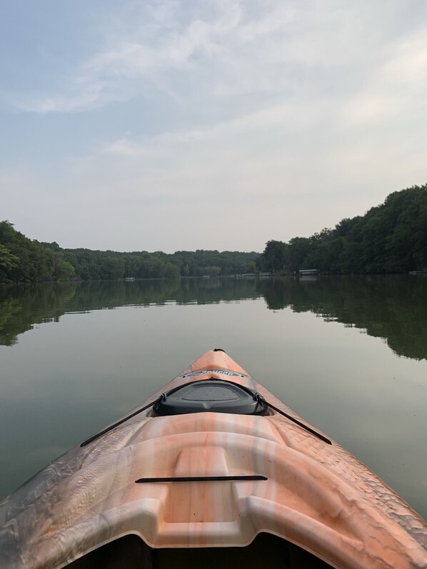 Un kayak sur une étendue d’eau calme, avec une rive boisée en arrière-plan.