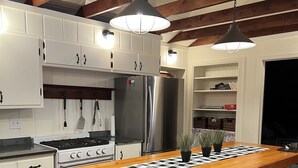 A modern kitchen with white cabinetry, a central island with stools, a stainless steel refrigerator, and a wooden ceiling.