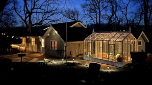 A house with a large glass greenhouse, a wooden deck, and a well-lit exterior.