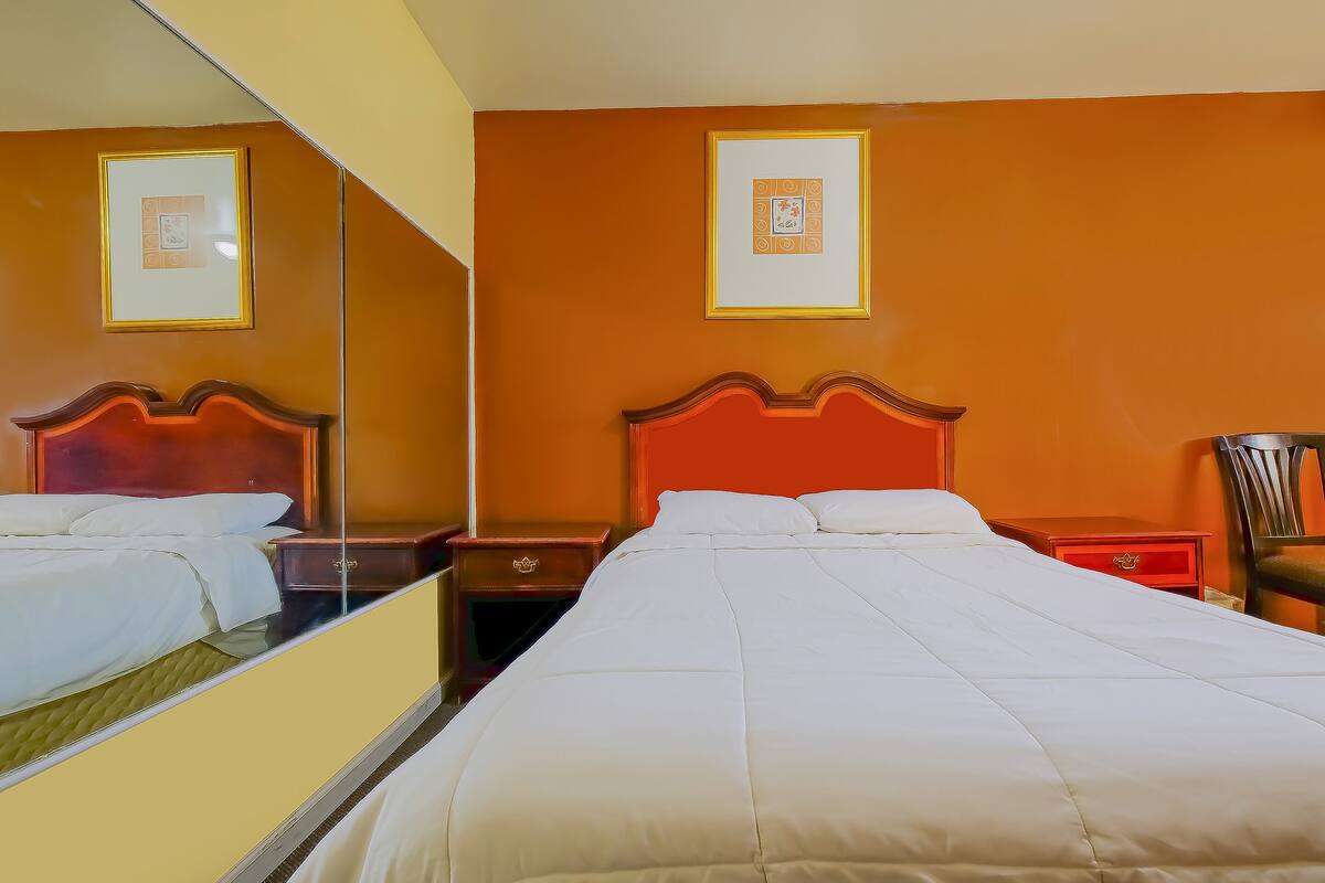 A hotel room with a large bed, a nightstand, a chair, and a mirror.