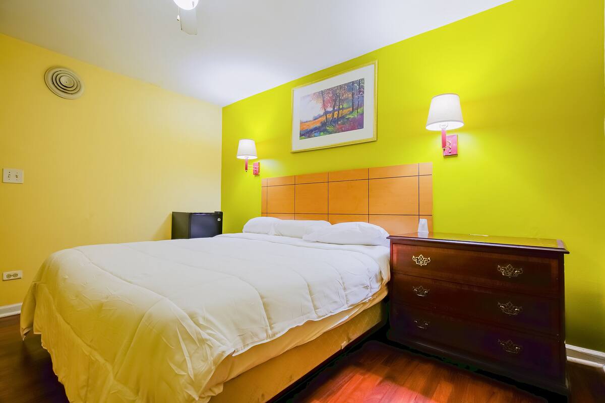 A hotel room with a bed, a dresser, a nightstand, and a painting on the wall.