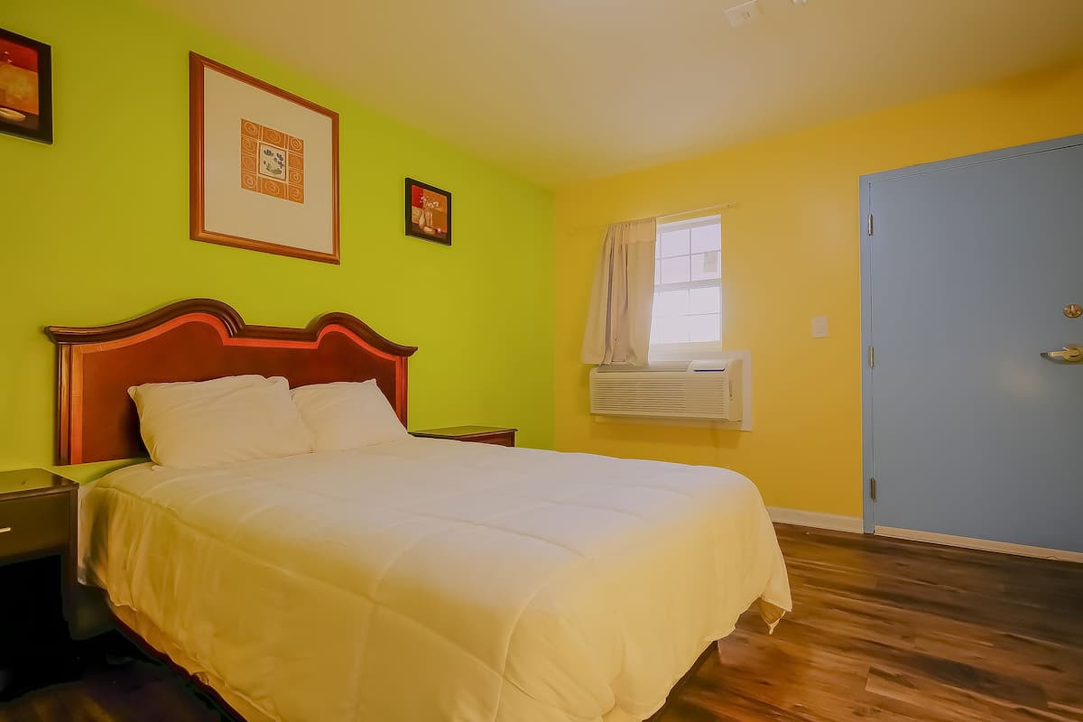 A bedroom with a bed, a nightstand, a wall-mounted air conditioner, and a door.