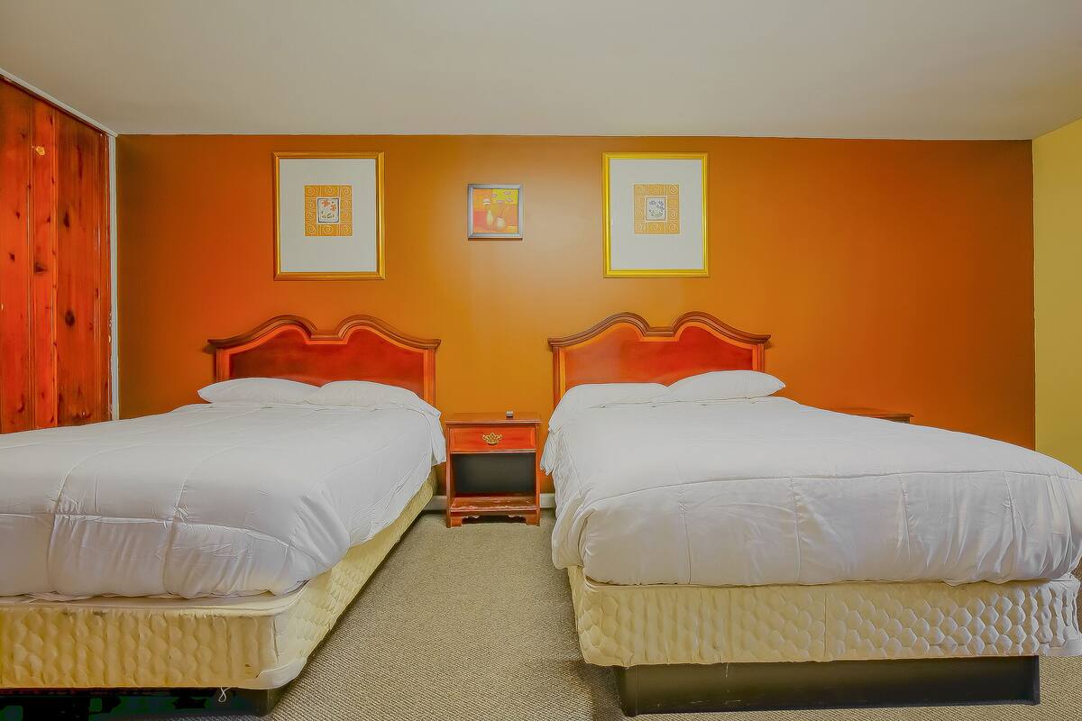 A hotel room with two beds, a wooden wardrobe, and two framed pictures on the wall.
