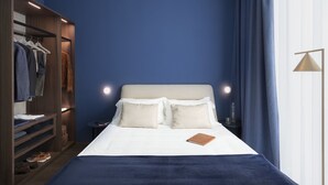 A bedroom with a bed, bedside lamps, a nightstand, a wardrobe, and a blue curtain.
