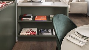 A modern living room with a staircase, a sofa, a dining table, and a bookshelf.