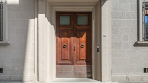 A double wooden door with a small window above it, set in a building with a light-colored stone facade.