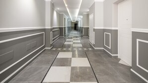 A long, narrow hallway with a checkered floor pattern, white trim, and a series of doors on one side.
