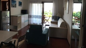 A compact living space with a kitchenette, a sofa, a dining table, and a view of the outdoors. - Bilocale Vista Mare (San Teodoro)