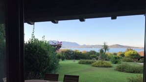 A patio with a round table and chairs, overlooking a well-maintained garden with various plants and a view of the sea and mountains in the distance. - Bilocale Vista Mare (San Teodoro)