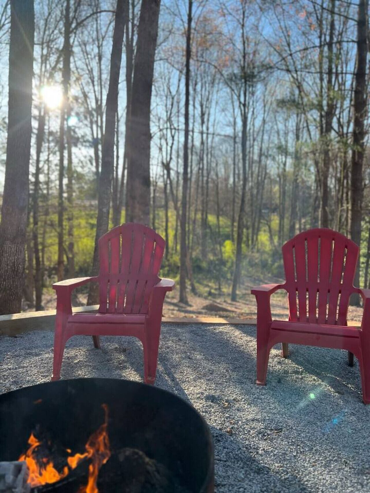 Deux chaises Adirondack rouges sont placées face à un foyer, dans un cadre forestier.