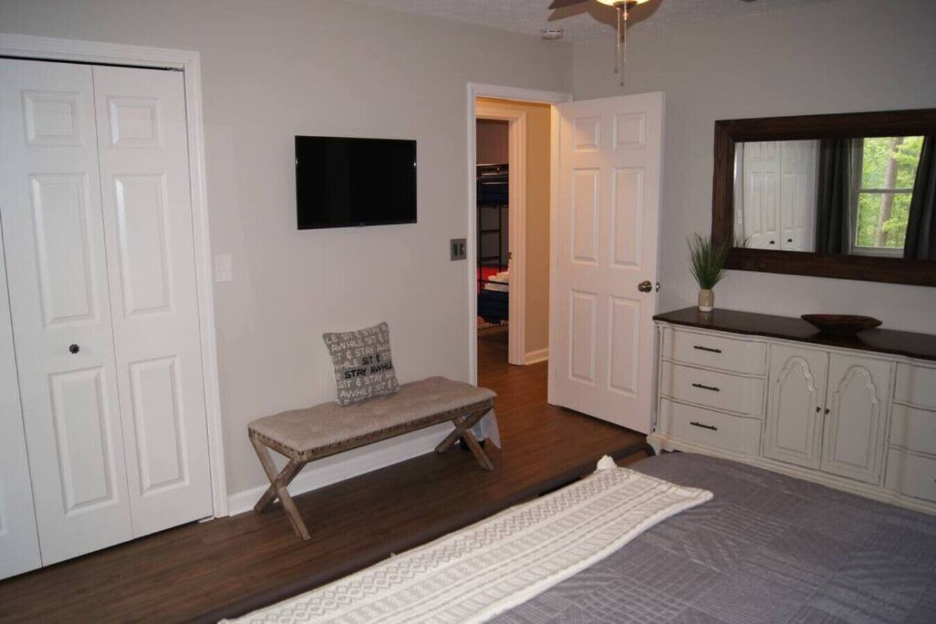 A hallway with a bench, a television mounted on the wall, a door leading to a closet, and a mirror above a cabinet.