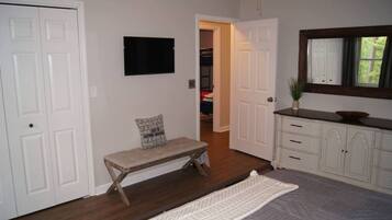 A hallway with a bench, a television mounted on the wall, a door leading to a closet, and a mirror above a cabinet.