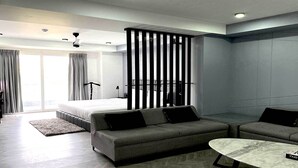 A modern hotel room with a bed, two sofas, a coffee table, and a large window with curtains. - Bedchambers Serviced Apartments, MG ROAD (Gurugram)