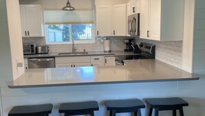 Una cocina moderna con armarios blancos, una isla grande con taburetes de bar y un ventanal que proporciona luz natural.