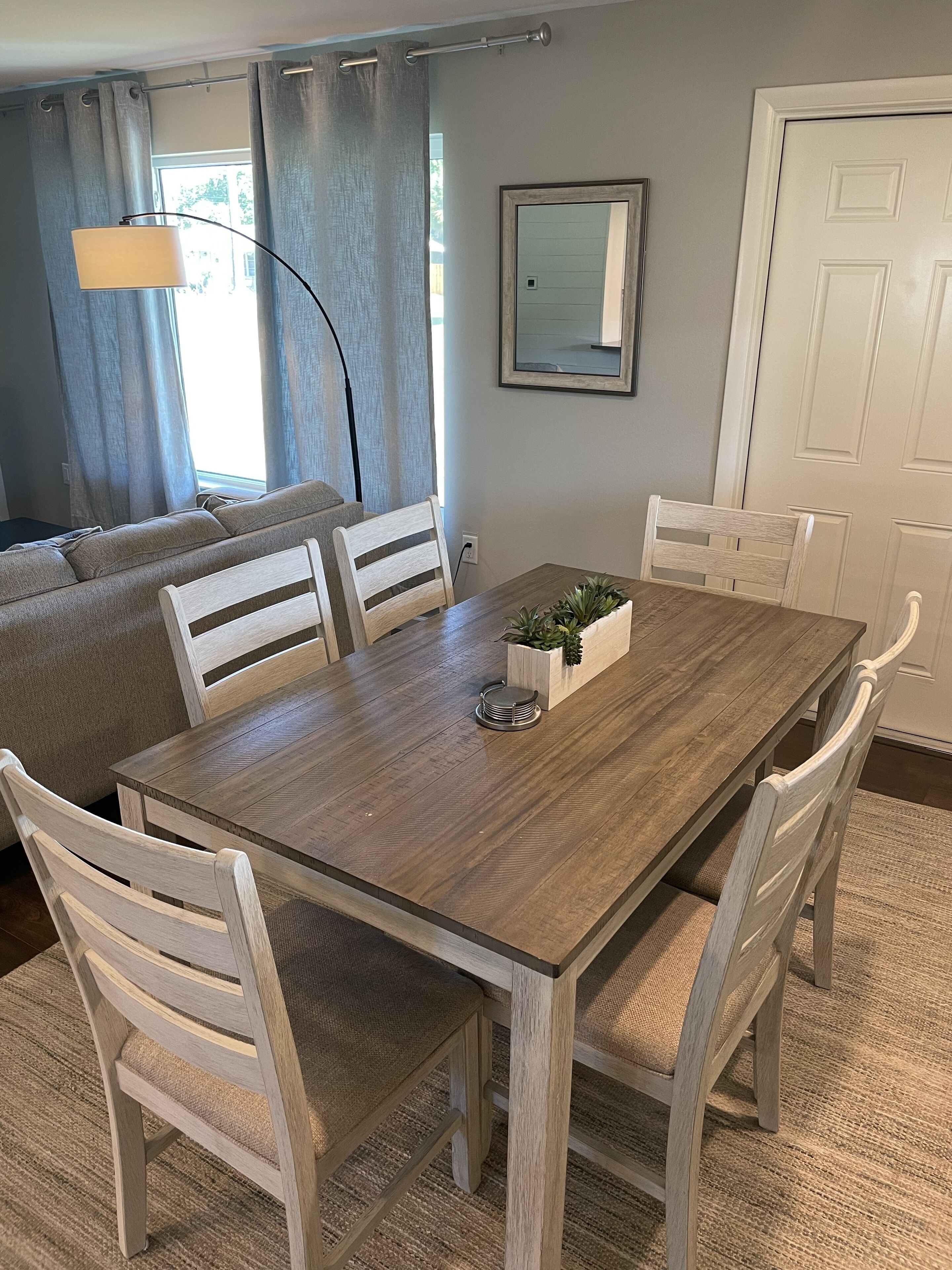 A dining area with a wooden table, white chairs, a small plant, and a mirror on the wall.