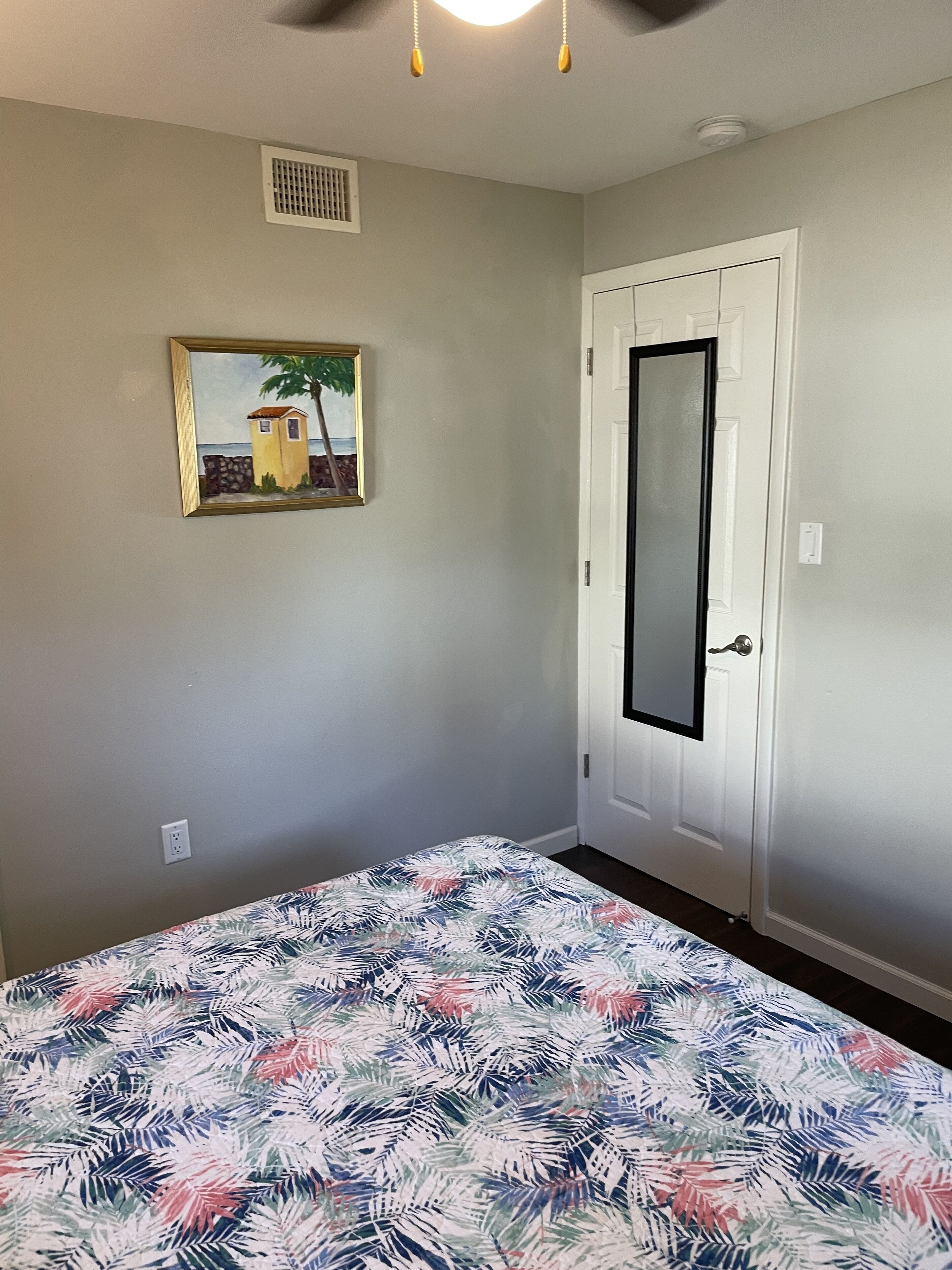 Ein Schlafzimmer mit Bett, Tür, Deckenventilator und Wandlüfter.