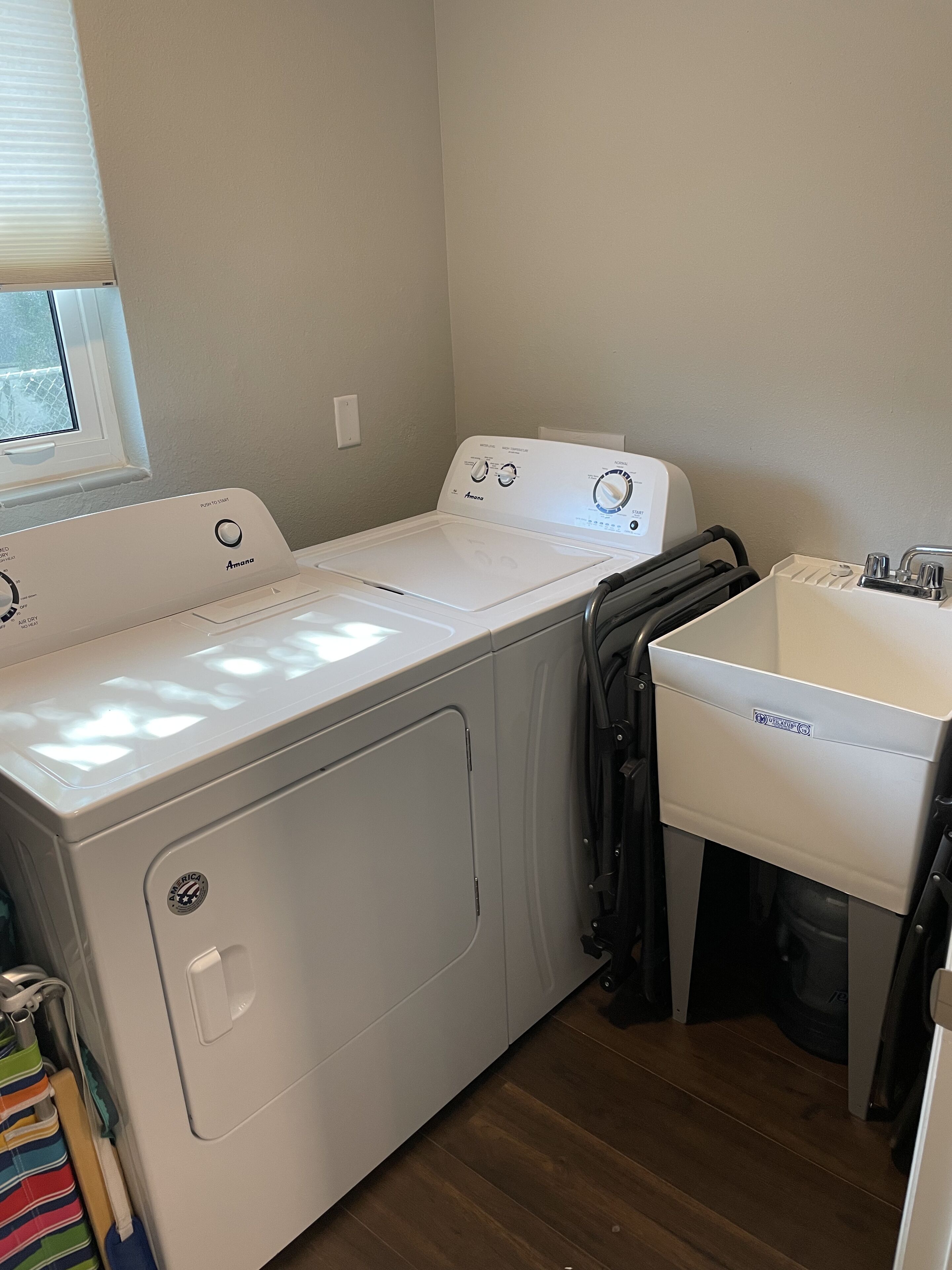 Un espace buanderie équipé d’un lave-linge et d’un sèche-linge à chargement frontal, d’un évier et d’une fenêtre avec des stores.