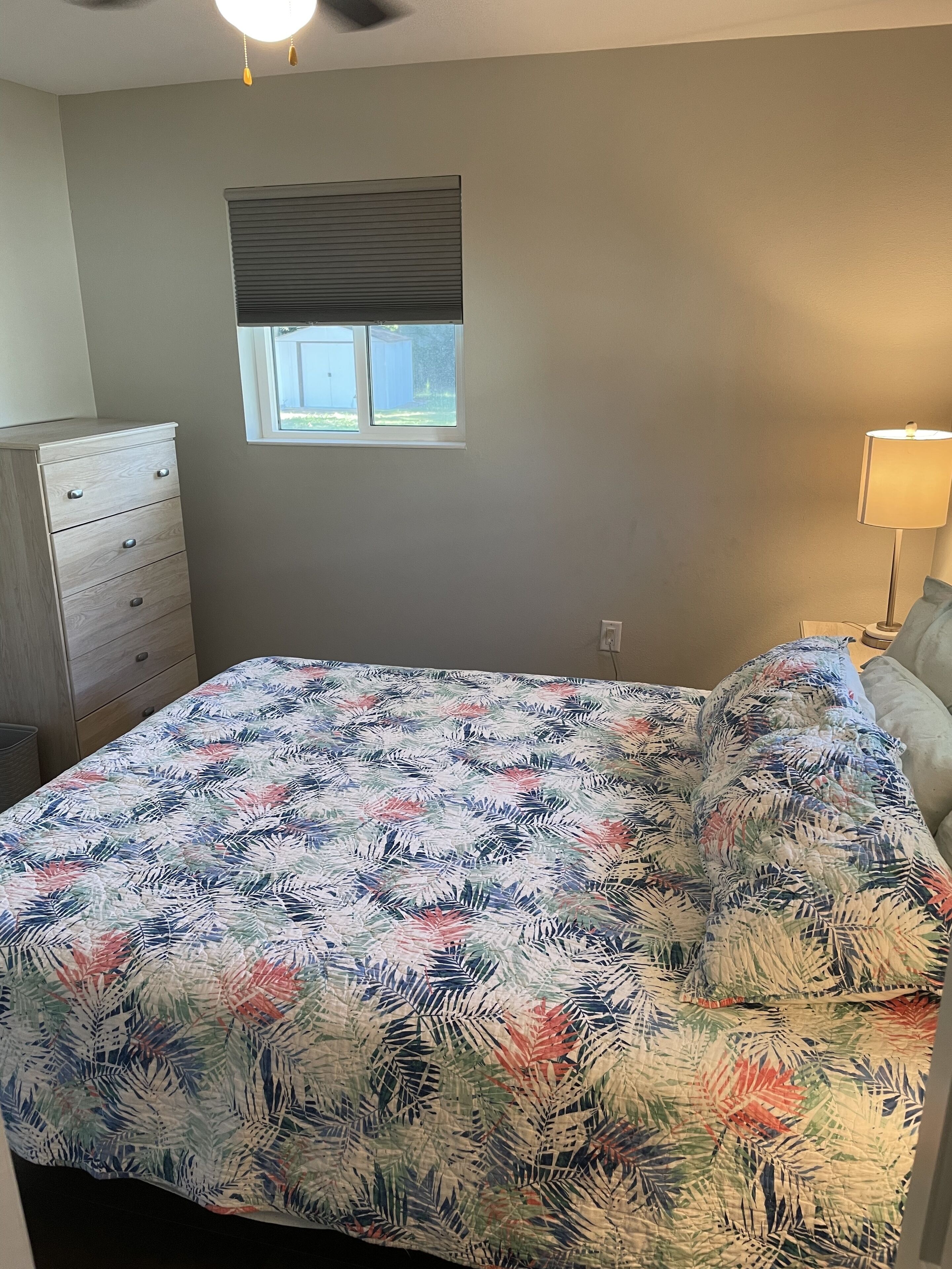 A bedroom with a bed, a dresser, a window, and a lamp.