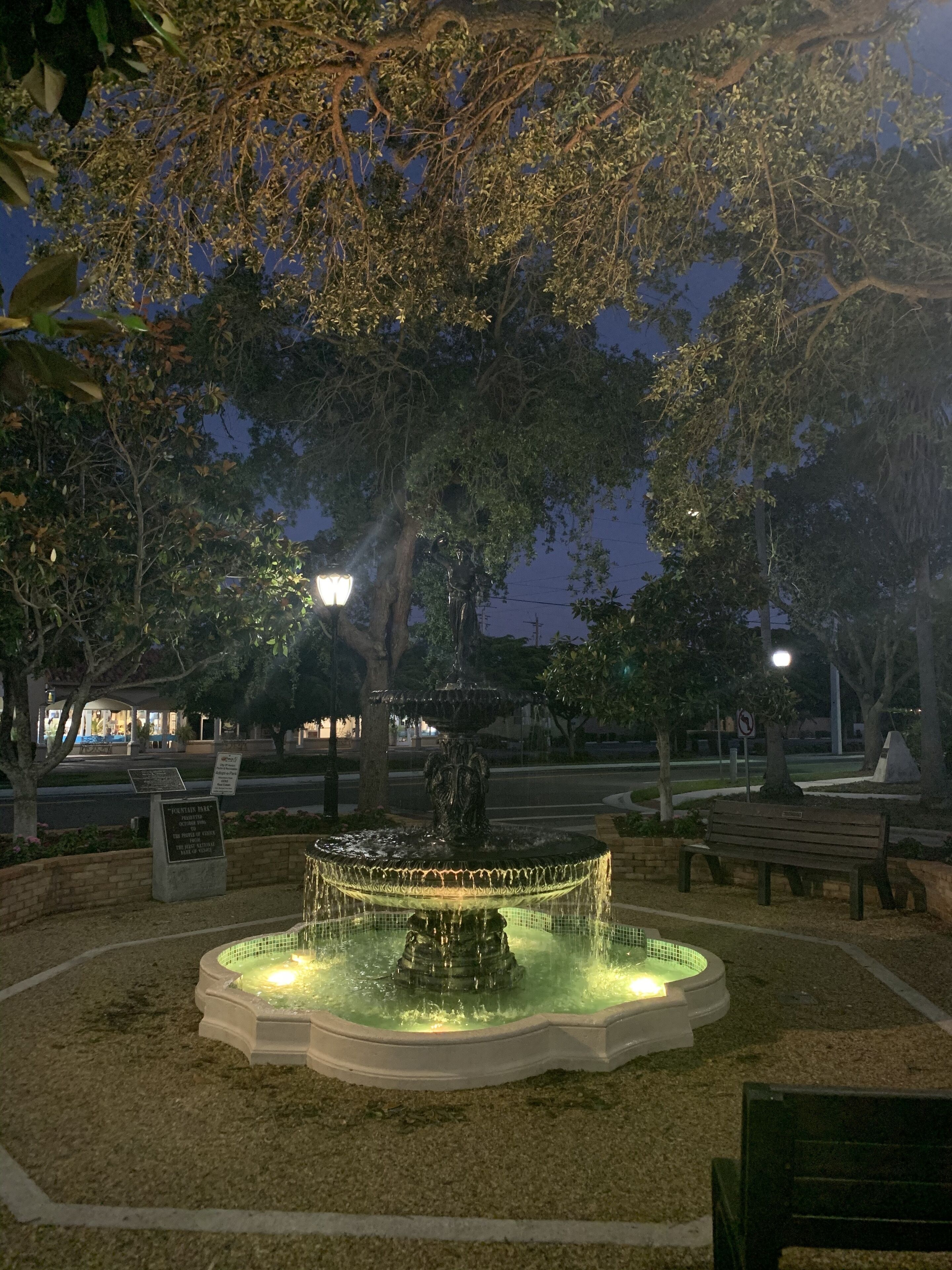 A park with a fountain, benches, and trees.