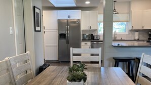 Una cocina moderna con armarios blancos, un refrigerador de acero inoxidable y un comedor con una mesa y sillas de madera.