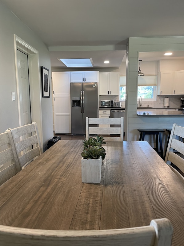 A modern kitchen with white cabinets, a stainless steel refrigerator, and a dining area with a wooden table and chairs.