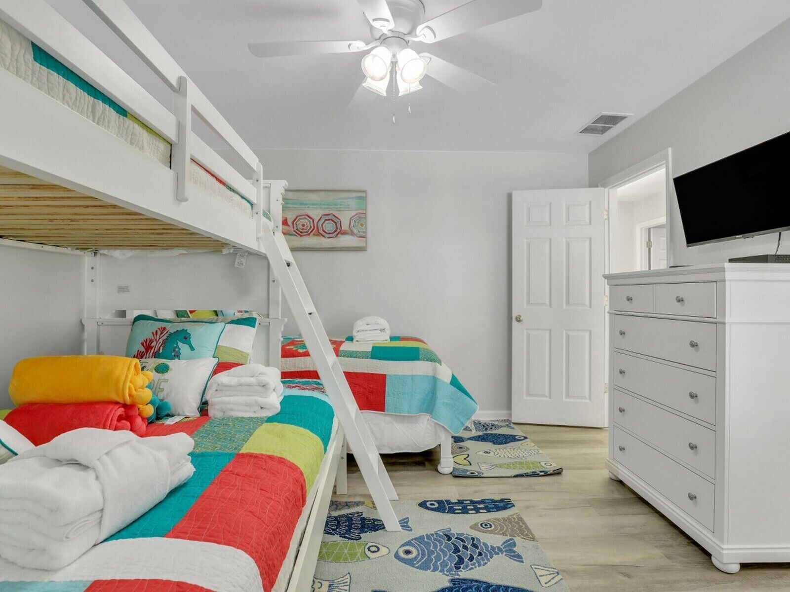 A bunk bed room with a ceiling fan, a white dresser, and a television on a stand.