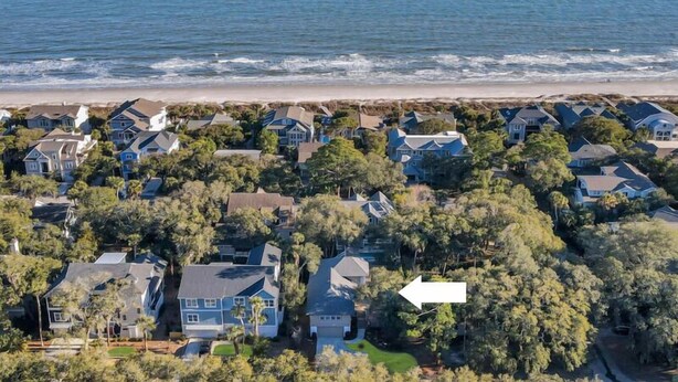 An aerial view of a coastal residential area with houses surrounded by trees and a beach in the background.