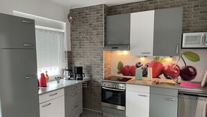 A modern kitchen with grey cabinets, a brick accent wall, and a fruit-themed backsplash.