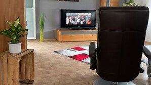 A modern living room with a flat-screen TV, wooden furniture, and a red and white rug.