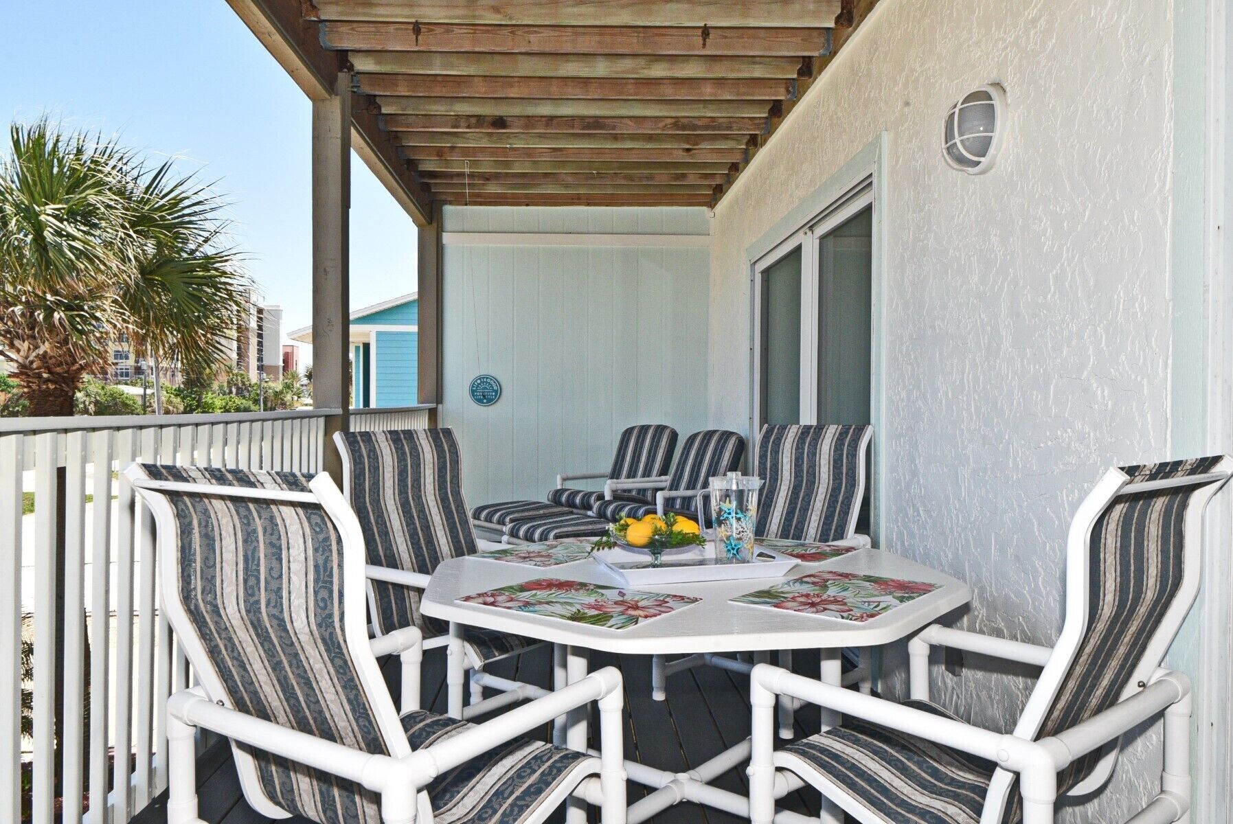 Eine überdachte Terrasse mit weißen Korbmöbeln und einem Tisch, gedeckt mit einer blumigen Tischdecke.